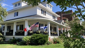 Une maison à deux étages avec un porche, des drapeaux américain et italien, et un jardin bien entretenu.