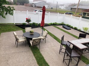 Eine Terrasse mit einem runden Tisch und Stühlen, einem roten Sonnenschirm und einem weißen Zaun.