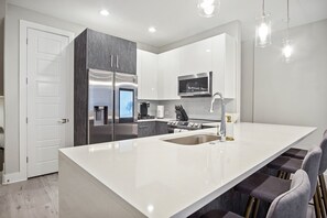 A modern kitchen with a large island, stainless steel appliances, and pendant lighting.