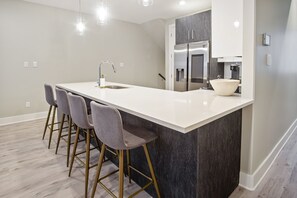 Una cocina moderna con una isla grande, taburetes de bar, electrodomésticos de acero inoxidable y un salpicadero de mármol.