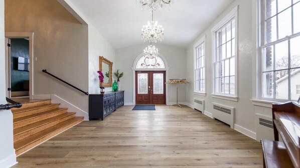 Ein geräumiger Flur mit Holzboden, einer imposanten Treppe und einer großen Chandelüster.