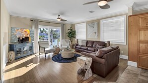 A spacious living room with a brown leather sofa, a television on a cabinet, and a ceiling fan. - Winter Getaway by the Bay. Direct Water View! Near Marco Island Beaches. (Naples)
