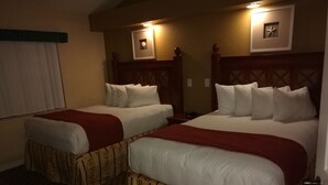 A hotel room with two beds, each with white linens and red blankets. There are wall-mounted lights above each bed, and a small decorative item on the wall. - Westgate Vacation Villas Resort (Kissimmee)