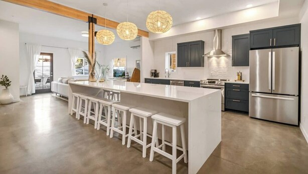 A modern kitchen with a large island, bar stools, stainless steel appliances, and pendant lighting.