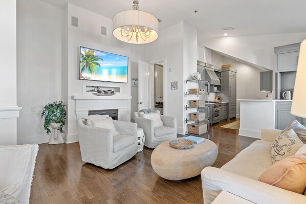 A modern living room with a fireplace, comfortable seating, a television, and a kitchen in the background.