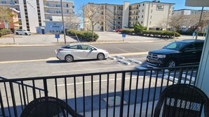 Ein Balkon mit Korbstühlen, der auf eine Straße mit geparkten Autos und Gebäuden im Hintergrund blickt.
