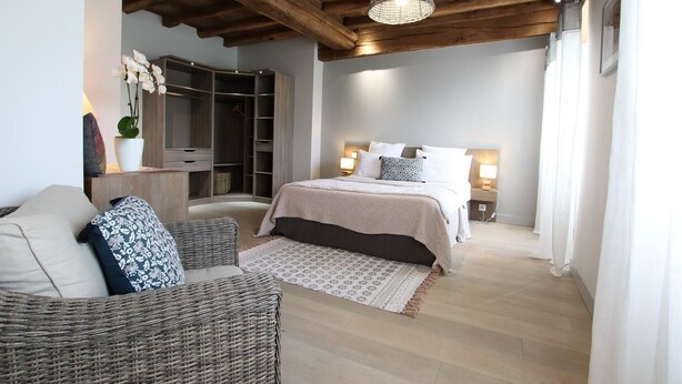 Ein Schlafzimmer mit Bett, Nachttischen, einem Kleiderschrank und einem Korbstuhl.