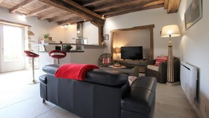 Ein Wohnzimmer mit einem schwarzen Ledersofa, einer roten Decke, einem Fernseher, einer Lampe und einer Küchenzeile mit einem Herd und einer Pflanze.