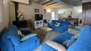 Un saló amb dos sofàs blaus, una televisió, una llar de foc i una zona de menjador amb taula i cadires.