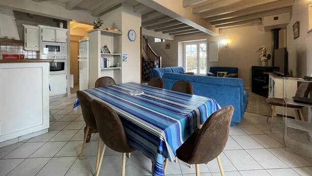 Una cuina àmplia amb armaris blancs, taula de dinar amb mantell rayat i un sofà blau a la zona de sala d'estar.