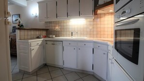 Una cuina compacta amb armaris blancs, forn integrat i una cantonera revestida de rajoles.