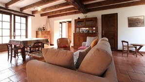 Una sala de estar acogedora con sofá, mesa de comedor y sillas. Hay un aparador de madera con puertas de cristal y un cuadro en la pared.