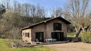 Una casa de piedra con techo inclinado, dos contraventanas negras y un pequeño patio con mesa y sillas.
