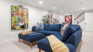 Ein modernes Wohnzimmer mit einem blauen Ecksofa, einem Couchtisch und einem großen, abstrakten Gemälde an der Wand.