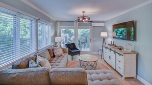 A modern living room with a sectional sofa, a round coffee table, and a dining area with a cabinet and a TV. - Totally remodeled Oceanfront Villa! New Owner! (Hilton Head Island)