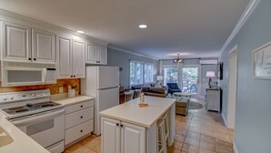 A modern kitchen with white cabinetry, a central island, and a dining area with a sofa and chairs. - Totally remodeled Oceanfront Villa! New Owner! (Hilton Head Island)