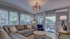 A modern living room with a sectional sofa, a round coffee table, and a balcony with outdoor furniture. - Totally remodeled Oceanfront Villa! New Owner! (Hilton Head Island)