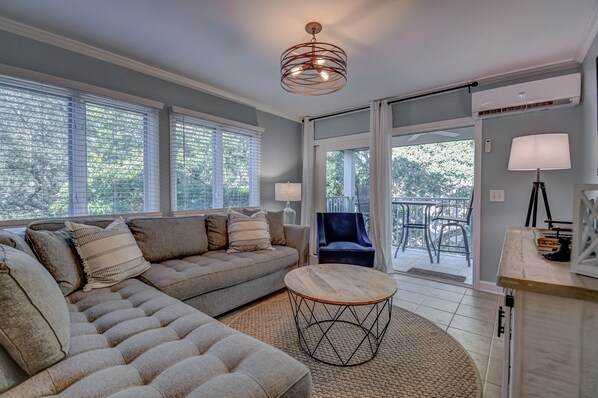 A modern living room with a sectional sofa, a round coffee table, and a balcony with outdoor furniture.