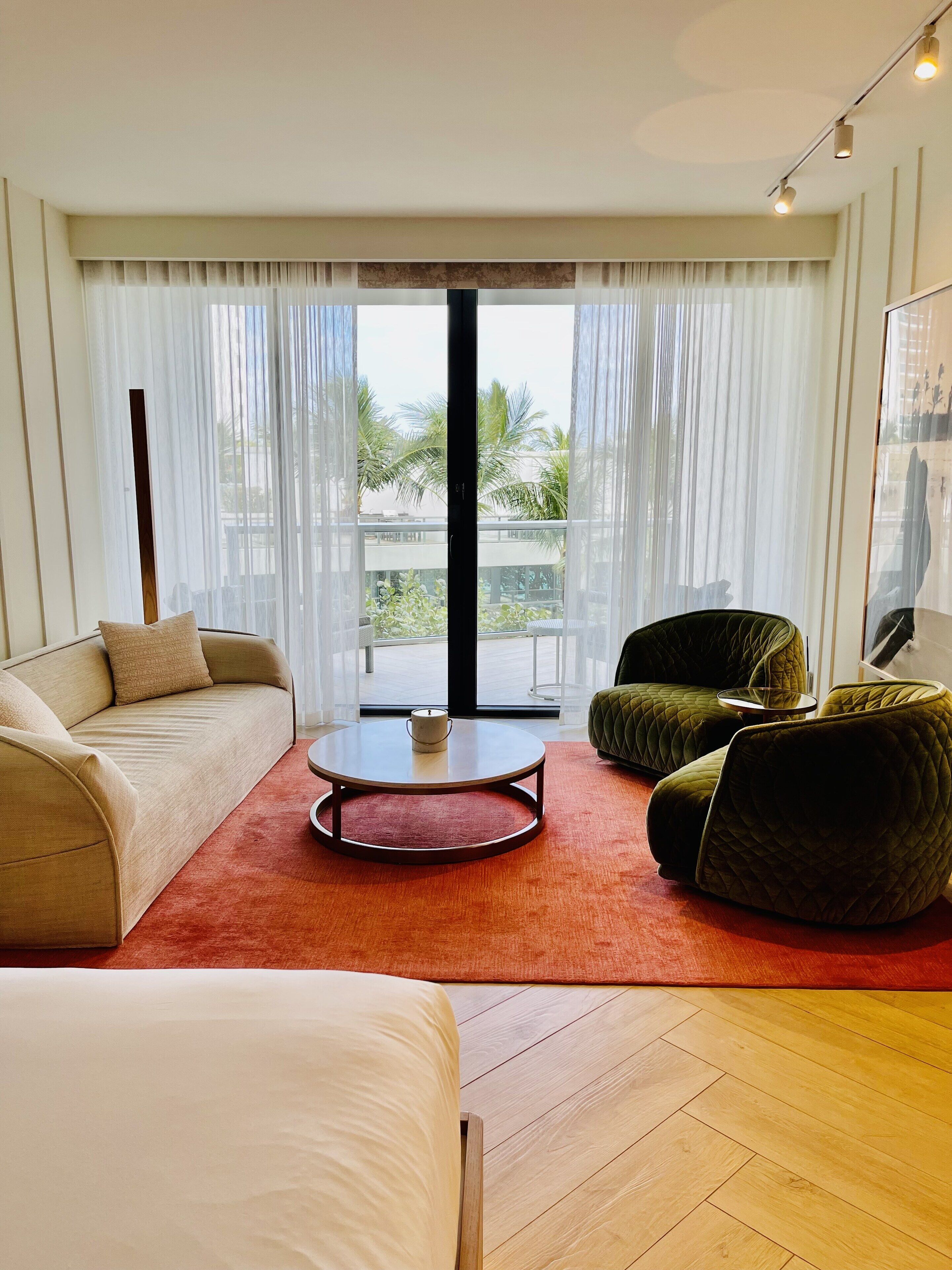 A modern living room with a sofa, a green armchair, a coffee table, and a large window with sheer curtains.