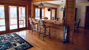 A wooden interior with a bar area, two bar stools, a rug, and a large mirror.