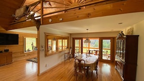 A spacious room with wooden floors, a dining table with chairs, a large window, and a wooden cabinet.