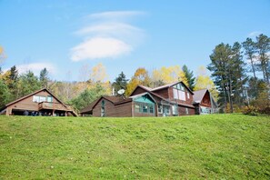 A row of wooden cabins with a grassy hill in the foreground and trees in the background.