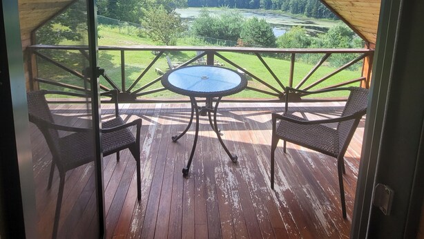 A wooden deck with a table and two chairs, overlooking a lush green landscape.