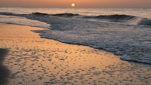 Una playa al atardecer con olas acercándose a la orilla.