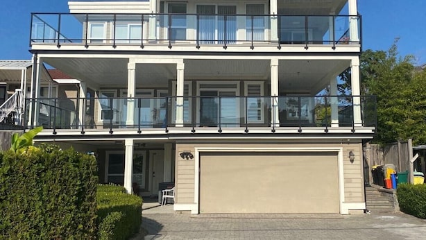 A two-story house with a garage, a balcony on the upper floor, and a covered front porch. - New two-bedroom legal suite with parking (White Rock)