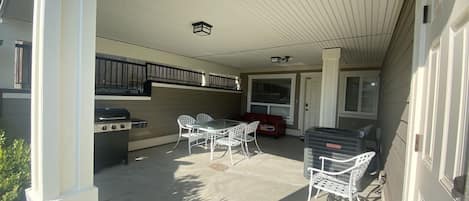 Un patio cubierto con una parrilla, asientos al aire libre y una puerta que da a la casa.