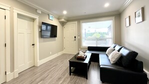 A modern living room with a black leather sofa, a coffee table, and a flat-screen TV mounted on the wall. - New two-bedroom legal suite with parking (White Rock)