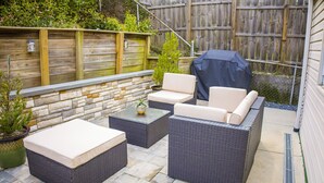 A patio area with wicker furniture, a stone wall, and a wooden fence.
