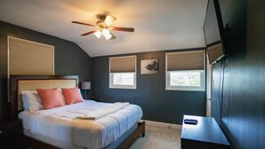 A bedroom with a bed, ceiling fan, windows, and a TV.