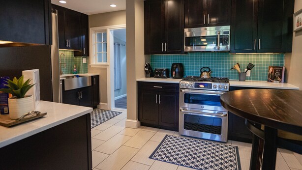 A modern kitchen with dark cabinets, stainless steel appliances, and a blue tiled backsplash.
