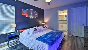 A bedroom with a bed, a ceiling fan, a nightstand, a lamp, a wall-mounted TV, and a bathroom visible through an open door. - Private Pool! Game room! Minutes to Disney! Themed rooms! (Kissimmee)