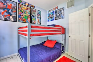 Habitación con literas, un colchón rojo y azul, una almohada roja y varios carteles de cómics en la pared.