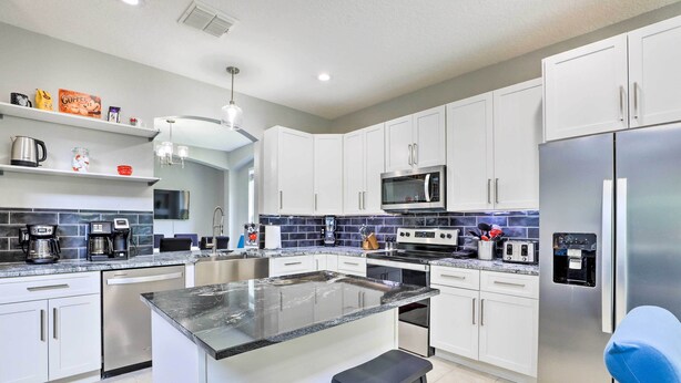 A modern kitchen with white cabinets, a central island, stainless steel appliances, and a blue backsplash. - Private Pool! Game room! Minutes to Disney! Themed rooms! (Kissimmee)