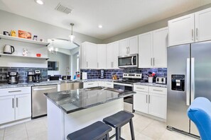 A modern kitchen with white cabinets, a central island, stainless steel appliances, and a blue backsplash. - Private Pool! Game room! Minutes to Disney! Themed rooms! (Kissimmee)