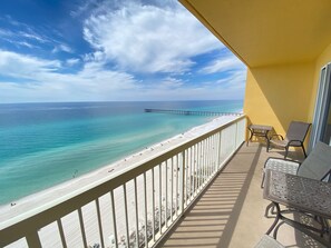 Un balcon avec vue sur la plage et lâocĂ©an, une jetĂ©e visible au loin et du mobilier dâextĂ©rieur.