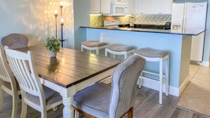 Een keuken met witte kasten, een houten eettafel en barstoelen.
