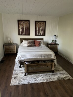 Une chambre à coucher avec un lit en bois, deux tables de chevet, un tapis et deux tableaux accrochés au mur.