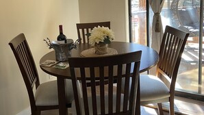 Un comedor con una mesa redonda, cuatro sillas de madera, una botella de vino y un cartel decorativo en la pared.