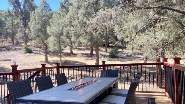 Terraza exterior con una mesa rectangular y sillas de mimbre, rodeada por una barandilla de madera.