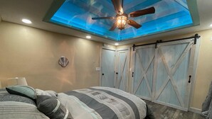A bedroom with a bed, a ceiling fan, and a skylight.