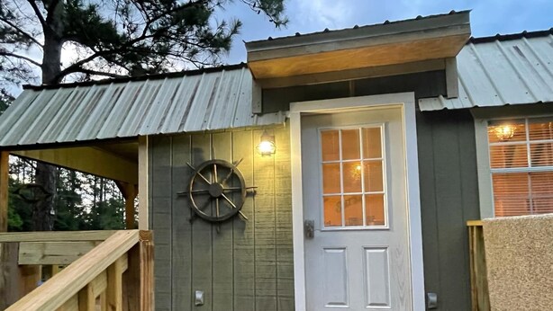 A wooden deck leading to a building with a white door and a clock on the wall.