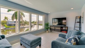 A modern living room with a large window, a flat-screen TV, a sofa, and a small table. - Boat Dock & Patio: Canal-Front St James City Home! (St. James City)