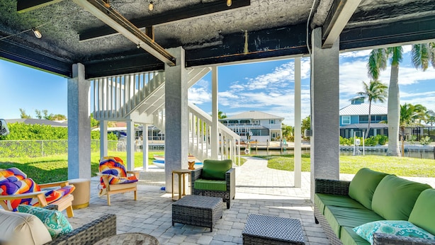 An outdoor patio area with wicker furniture, a green sofa, and a staircase leading to an upper level. - Boat Dock & Patio: Canal-Front St James City Home! (St. James City)