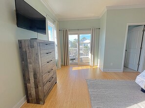 Um quarto espaçoso com cômoda de madeira, televisão de tela plana na parede e uma grande porta de vidro deslizante que dá para um deck externo.