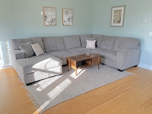 Um sofá modular cinzento com uma mesa de centro de madeira em uma sala de estar com parede azul clara e obras de arte emolduradas.