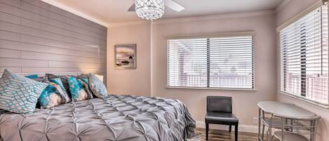 A bedroom with a tufted bed, a ceiling fan, a window with blinds, a chair, and a small table.